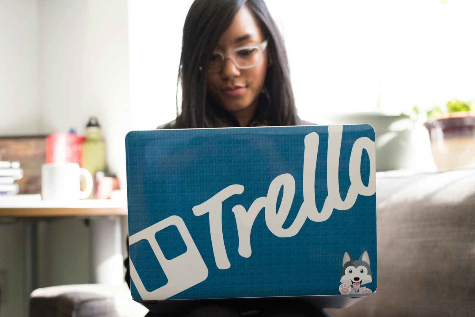 Focused woman engaged in remote work using a Trello-branded laptop in a cozy indoor setting.