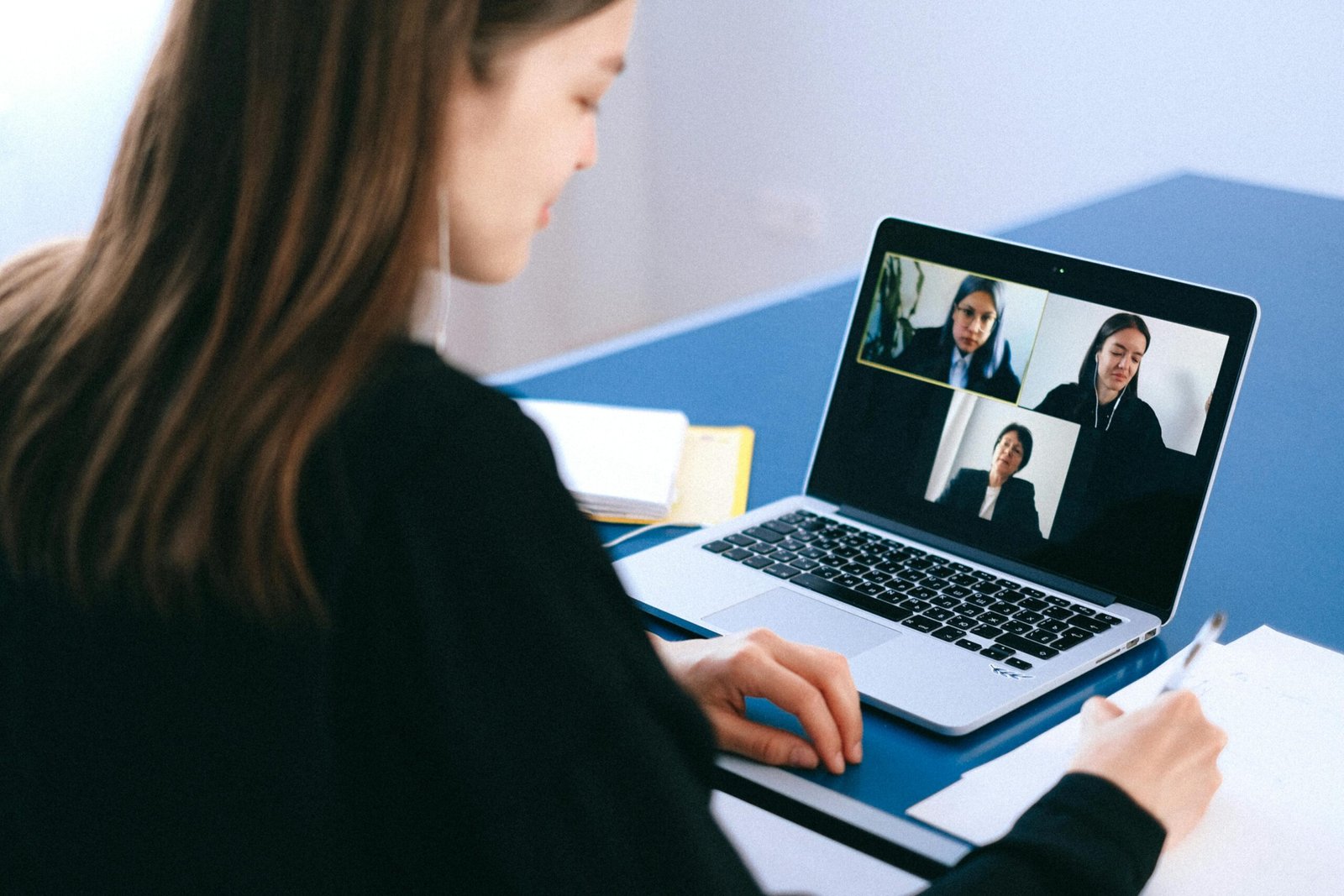 A woman engaging in a video conference using a laptop at home, taking notes.